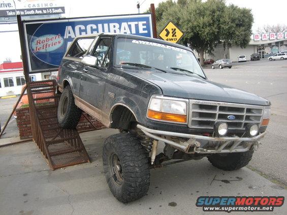 Dark green lifted Ford Bronco with off-road bumper and large tires on a metal ramp