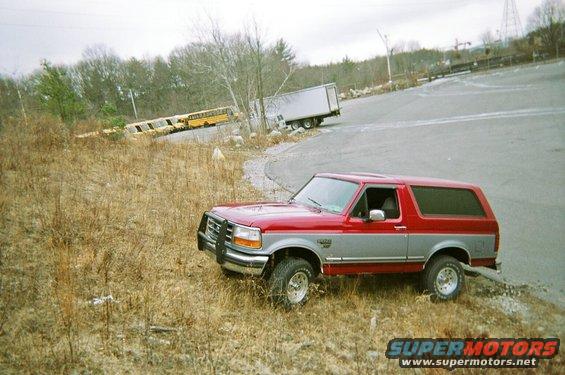 red and silver SUV parked on grassy slope, school buses and semi-trailer in background