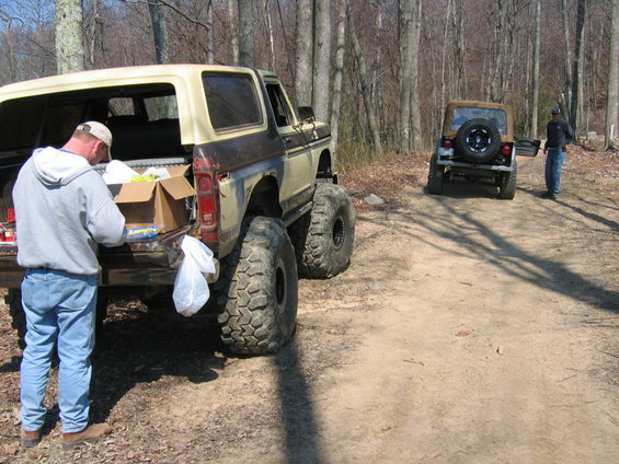 Modified 1978 Ford Bronco with oversized tires, rear view. A Jeep Wrangler is parked behind it on a dirt road