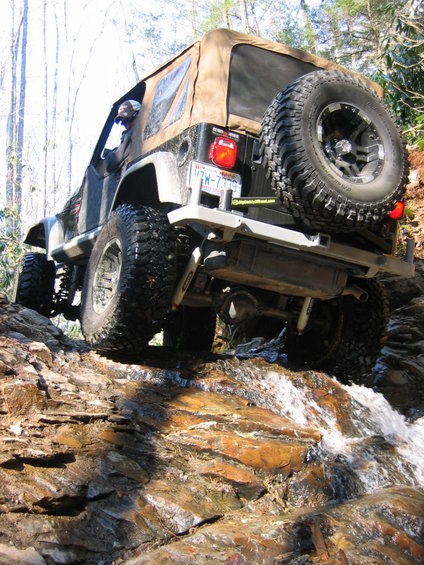 Jeep Wrangler driving over rocks and water on a trail