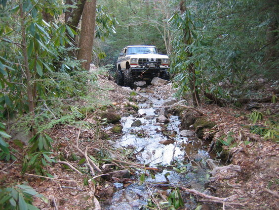 1978 Ford Bronco driving through a rocky stream in a forest