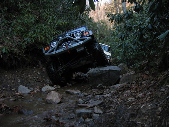 Jeep Wrangler navigating a rocky stream bed with another vehicle behind it