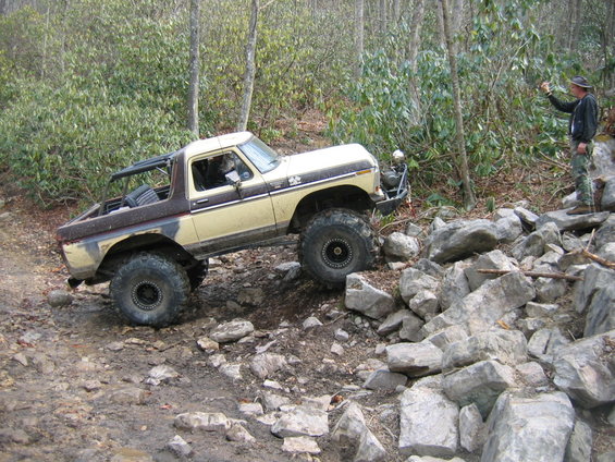 Off-road modified Ford Bronco climbing over rocks on a trail