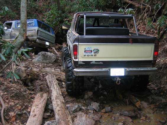 Rear view of a lifted Ford Bronco navigating a rocky, wooded trail