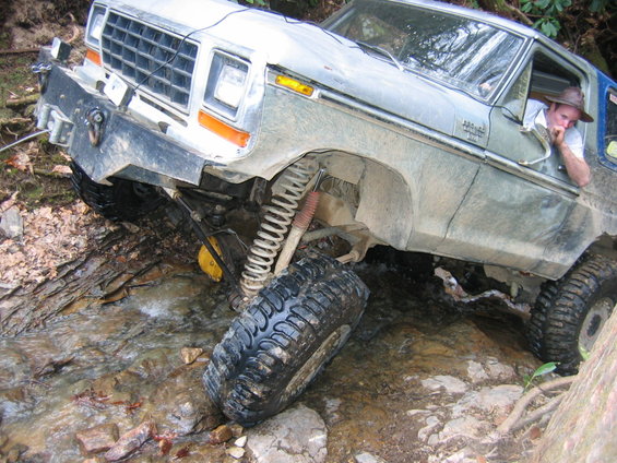 Silver off-road vehicle with large tires stuck in a rocky stream bed, front end angled up