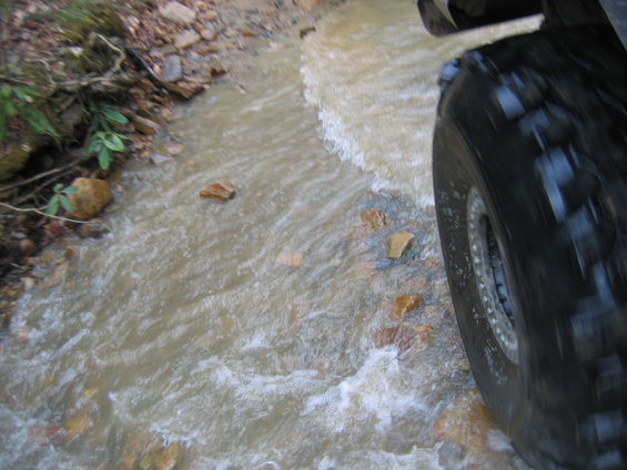 Tire of an off-road vehicle splashing through a shallow stream on a dirt path