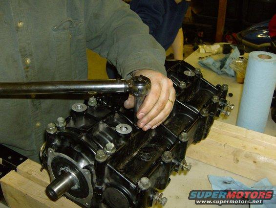 Black engine component with bolts and a shaft, being worked on with a wrench