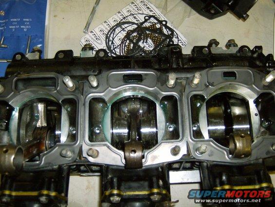 Engine block with pistons and crankshaft visible, gasket set in background