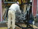 1978 Ford Bronco - Two mechanics work on an engine suspended from an engine hoist in a garage setting.