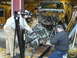 1978 Ford Bronco - Mechanics use an engine hoist to remove the powerplant from a disassembled Ford Bronco.