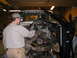 1978 Ford Bronco - Mechanics are using a crane to lift an engine out of a vehicle in a garage setting.