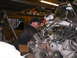 1978 Ford Bronco - Mechanic works on a complex engine assembly, possibly during an EFI swap, with a chain hoist overhead.
