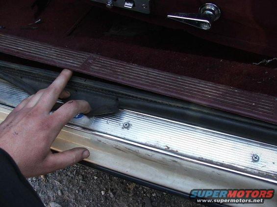 Hand touching the rubber weatherstripping on a car door sill