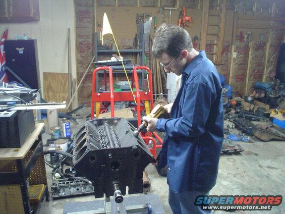 Man in blue shirt works on a black engine block on a stand in a garage