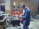 1976 Ford F-100 - A person is using a tool to work on an engine block in a cluttered garage setting.