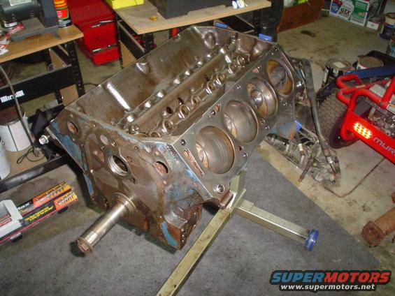 Engine block on a stand, showing cylinder bores and crankshaft snout. Rusty and blue paint visible