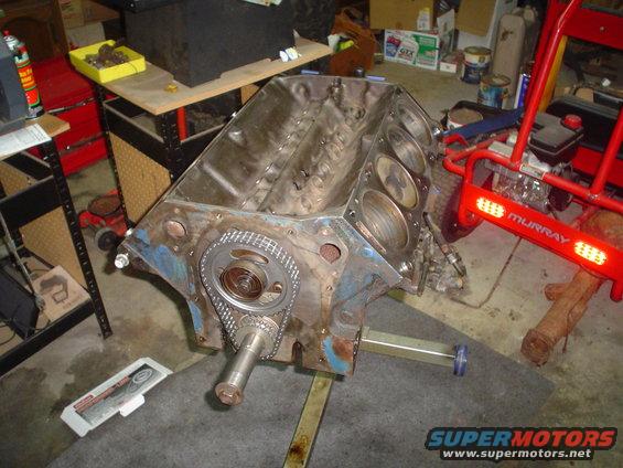 Engine block with timing chain and gears visible, resting on a stand in a garage