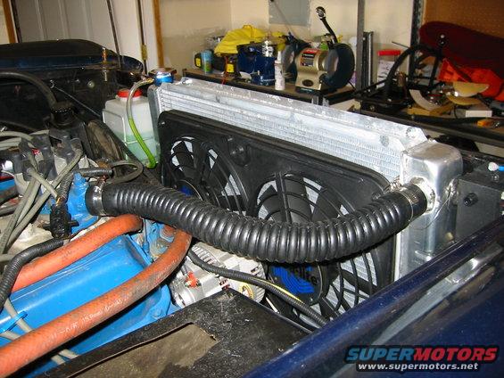 Engine bay showing a large aluminum radiator with dual electric fans, blue engine block, and orange hoses