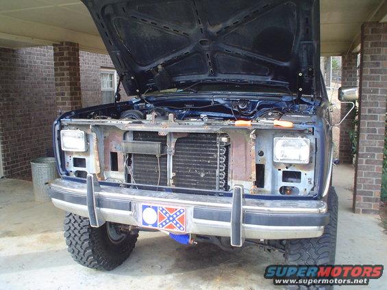 Front of a dark blue Ford truck with hood up, showing engine bay and radiator. Bumper has a Confederate flag decal