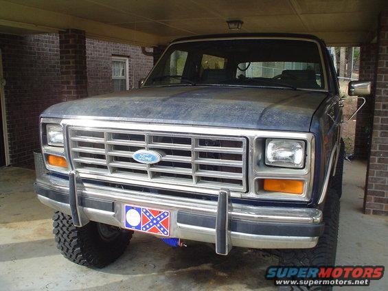 Blue Ford Bronco front view, showing grille and headlights. License plate frame has a Confederate flag