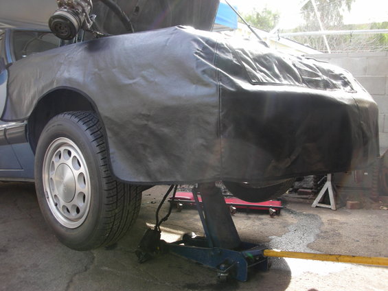 car front end covered, engine parts visible above, on jack stands