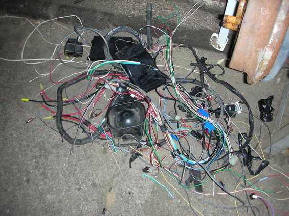 Tangled automotive wiring harness with black plastic connectors and various colored wires on a concrete floor