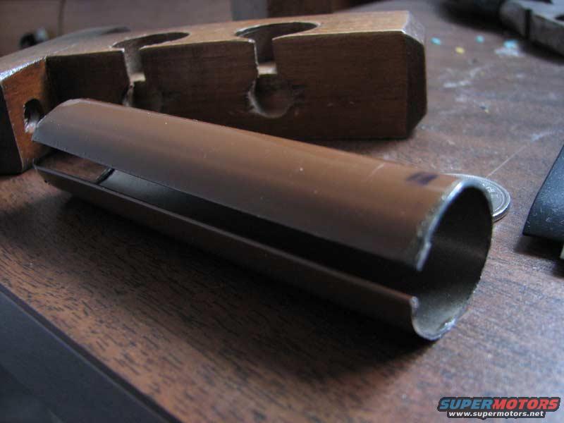 Brown metal pipe part with a cut end, resting on a wooden surface next to a wooden block