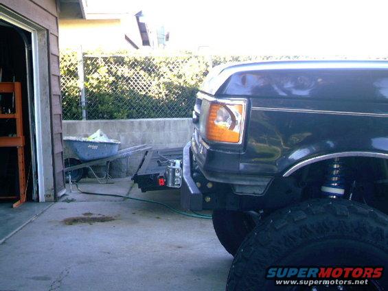Front bumper and fender of a dark 1989 Ford Bronco, showing the headlight and wheel well