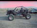 1984 Ford Bronco - Custom buggy with roll cage and racing seats sits on dirt. Another vehicle is on a trailer behind it.