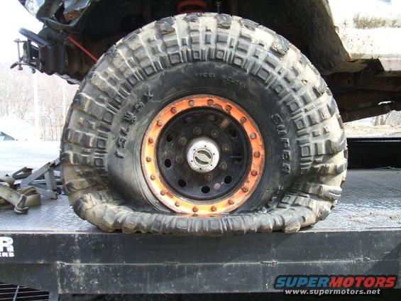 Flat off-road tire with orange rim on a trailer, showing damage