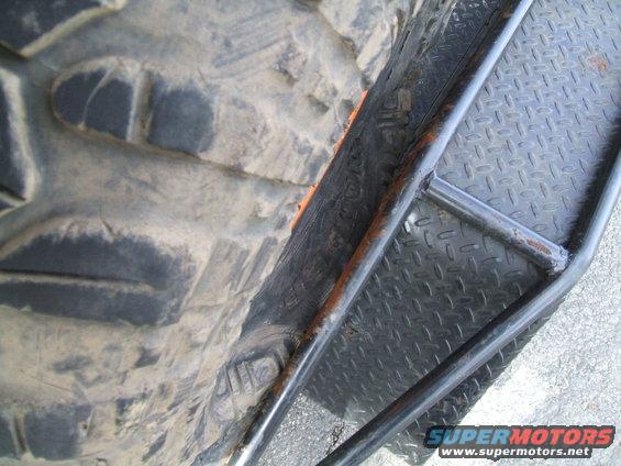 Close-up of a large off-road tire next to a diamond plate metal step with black metal bars