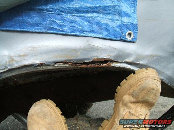 Rusted wheel well with blue tarp overhead and tan boots in foreground
