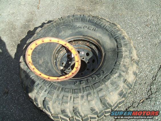 Off-road tire with a beadlock ring sitting on the tread. Tire has 'SWAMPER' text