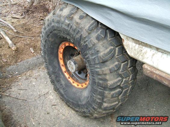 Off-road tire with orange beadlock on a vehicle covered by a gray tarp