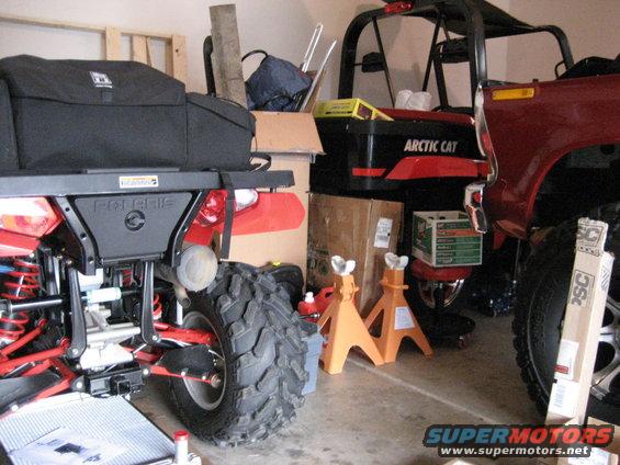 Red SUV and ATV parked in a garage with storage boxes and jack stands