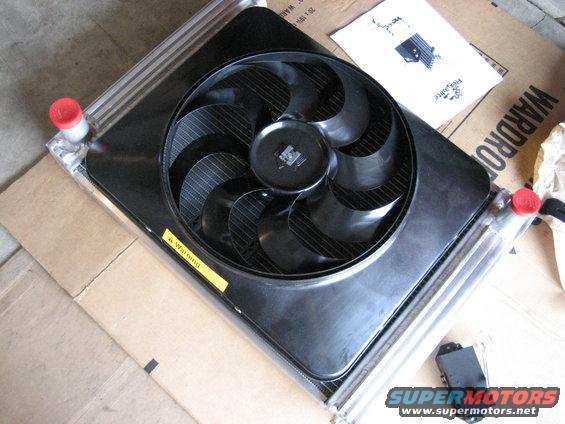 Radiator and fan assembly with red caps on inlet/outlet pipes, sitting on cardboard