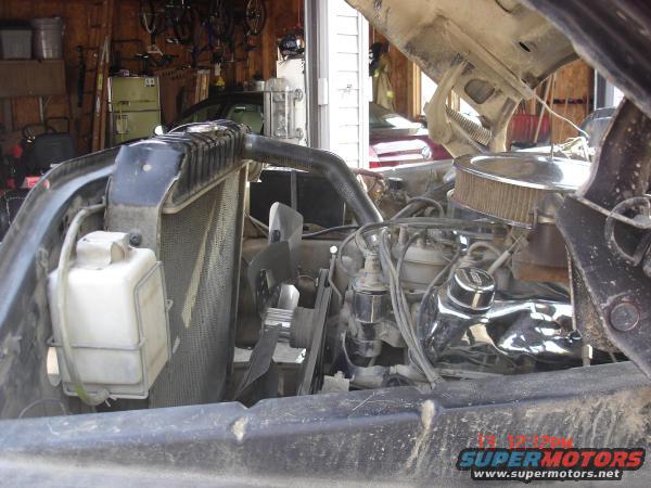 Engine bay showing radiator, fan, and engine components. Water reservoir is visible on the left