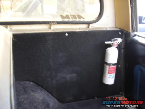Interior panel with a white fire extinguisher mounted on it. A partial reflection of text is visible on the rear window