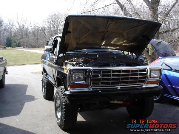 1979 Ford Bronco, front view, hood open showing engine. Another vehicle is partially visible to the right