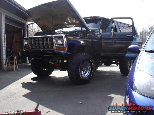 Black Ford Bronco with hood and door open, parked next to a blue car. Date stamp shows 13:12 5PM