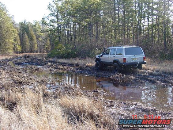 Silver Jeep Cherokee XJ navigating a muddy trail with snorkel