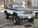 1994 Ford Bronco - A two-tone lifted Ford Bronco is parked on a paved surface with another vehicle partially visible to the right.