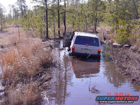 White Jeep Cherokee stuck in muddy water, driver's door open
