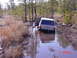 1995 Dodge 1500 - A white Jeep Cherokee navigates a muddy, water-filled trail with its driver's door ajar.