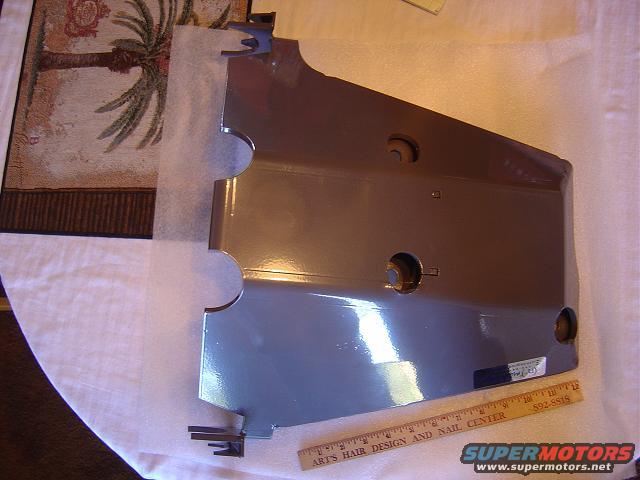 Gray engine cover part with some holes and mounting tabs. A ruler is next to it