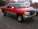 1994 Ford Probe - Red GMC Sierra pickup truck with a two-tone gray lower body is parked on a gravel lot.
