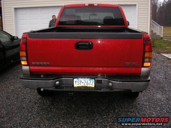 Red GMC Sierra pickup truck rear view with license plate YSP-2672. A man stands in the open garage door behind it