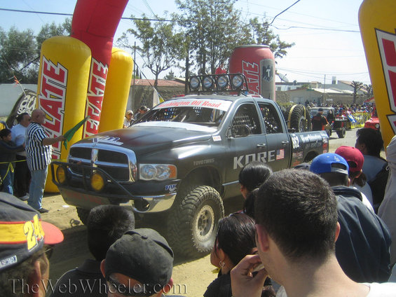 Black Dodge Ram pickup truck with KORE graphics, large off-road tires, and light bar on roof
