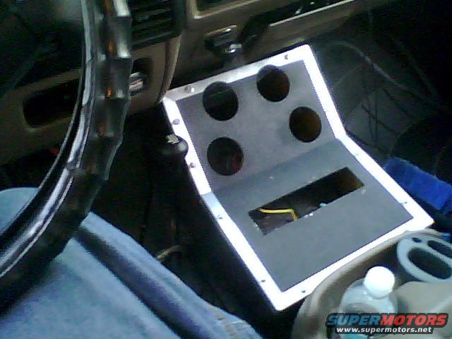 Custom center console with four circular cutouts and a rectangular opening, showing wiring. Steering wheel and part of dashboard visible