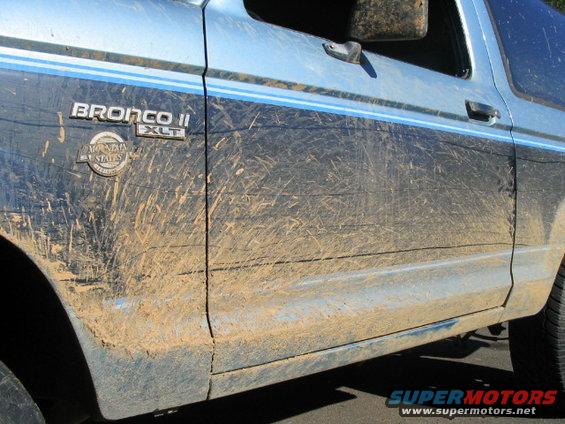 Side view of a blue Ford Bronco II covered in mud. It has a 'Bronco II XLT' badge and a 'Mountain States' emblem